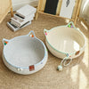 A woven cat scratcher and comfort bed with play balls resting on a light brown rug.