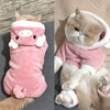 A fluffy cream-colored cat wearing a pink cartoon animal jumpsuit costume.