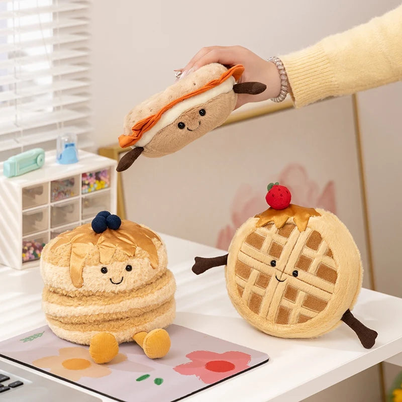 A hand is holding a fluffy, brown plush toy shaped like a sandwich, next to another rounder plush toy.