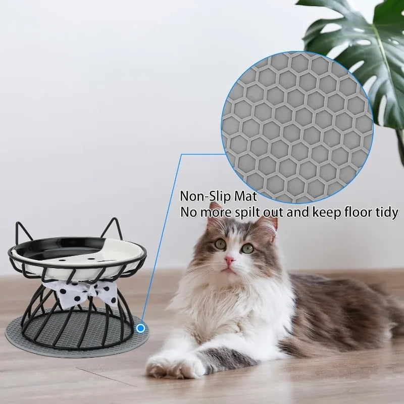 A fluffy gray and white cat is resting on a non-slip mat next to an elevated ceramic food dish designed for cats.