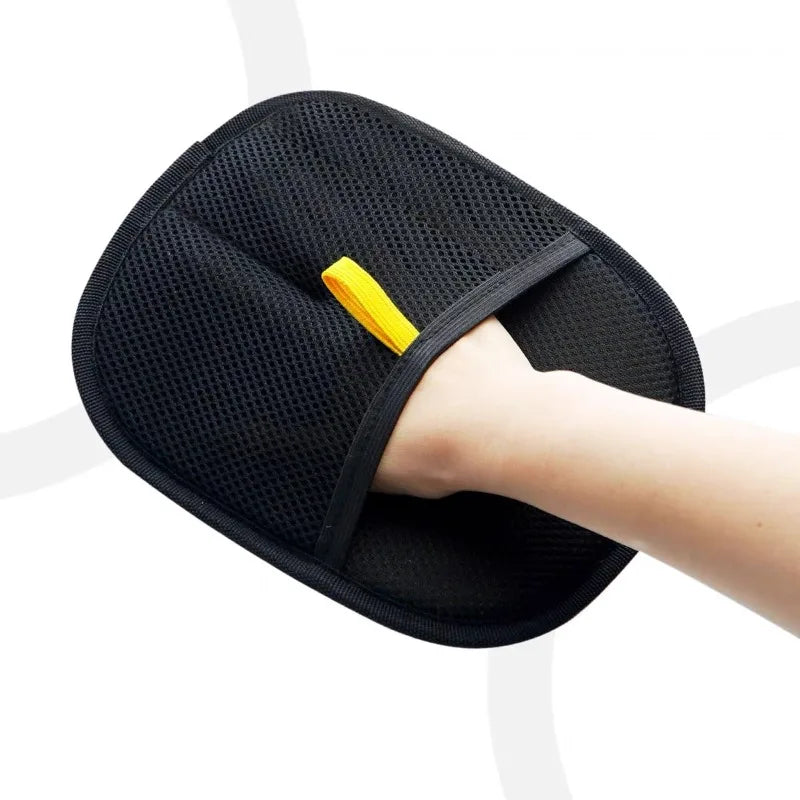A hand is using a black pet hair removal grooming glove with a yellow grip on a white background.