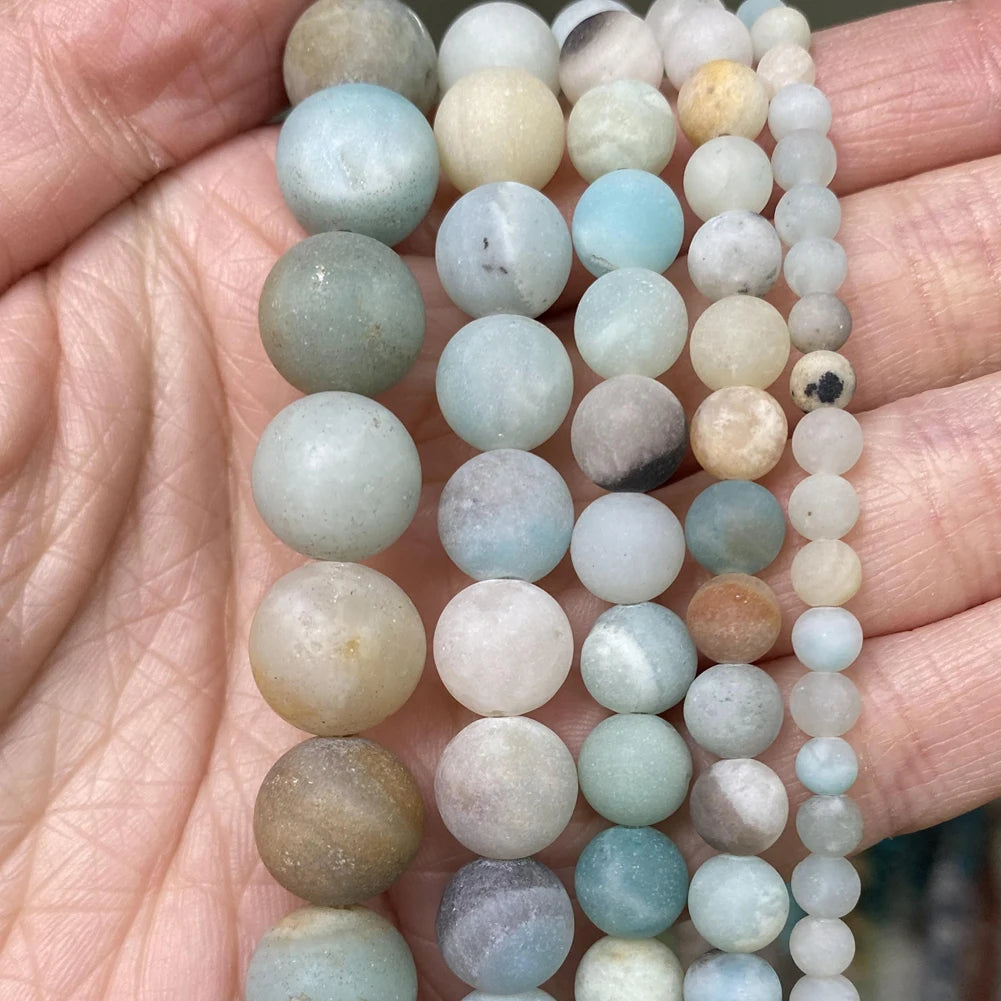 A string of natural stone beads in various shades of blue, green, and beige is held in a hand.