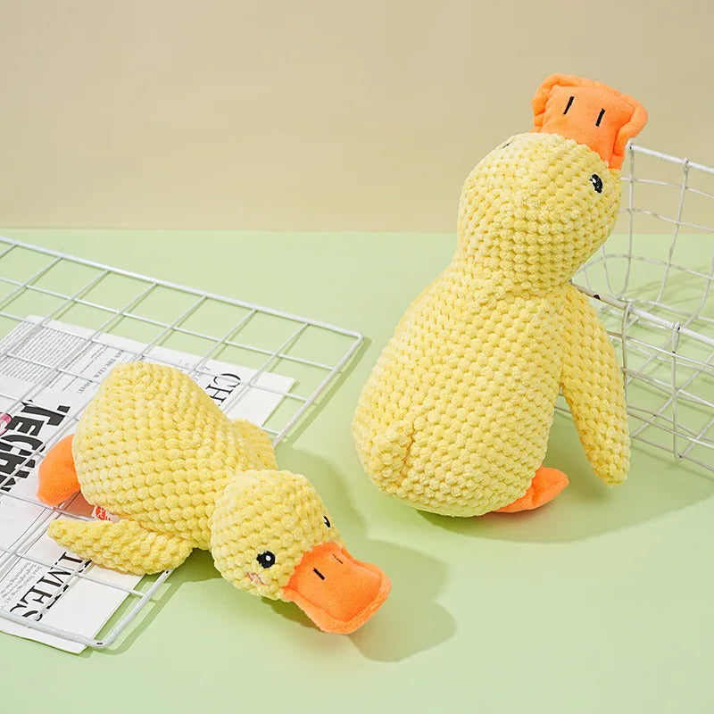 A yellow plush duck dog toy with orange accents is shown next to a wire mesh and some paper.