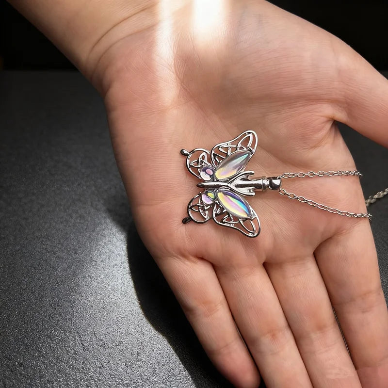 Silver butterfly ashes urn necklace worn on a person's hand.