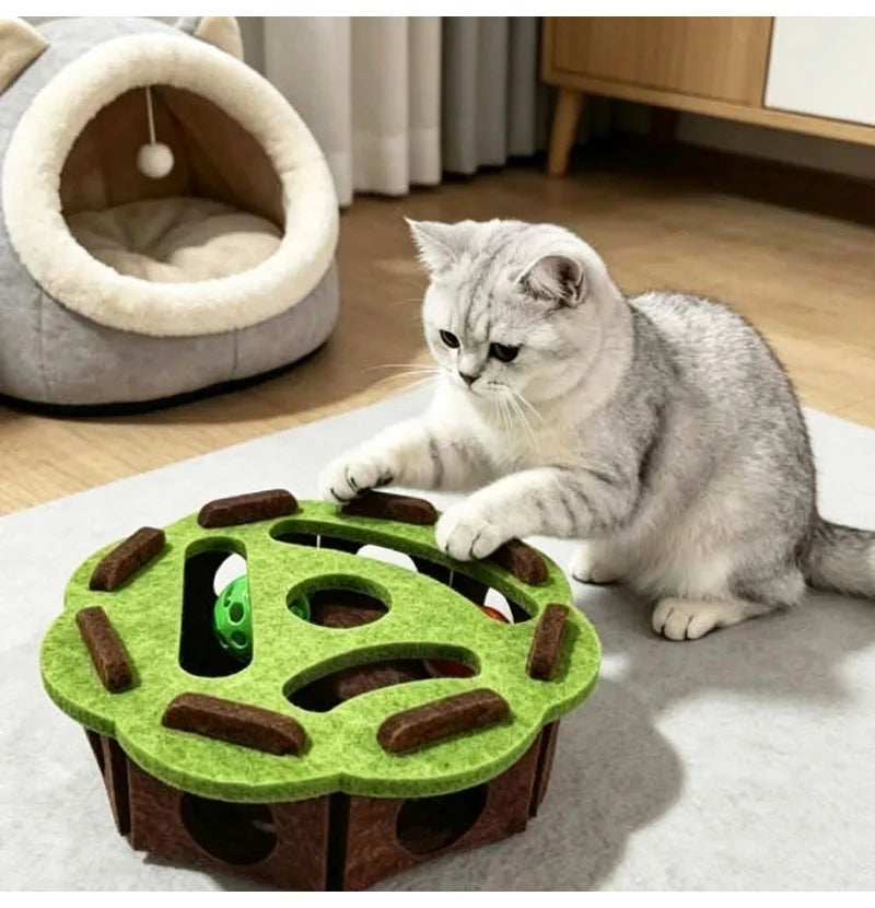 A gray cat is interacting with a green puzzle toy box designed for cats, featuring tunnels and a maze.