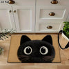 A cute black cat design bathroom mat with large eyes and whiskers placed on a wooden floor.