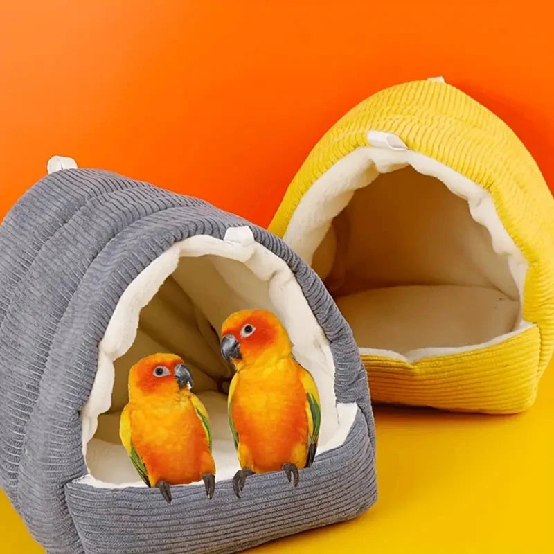 A gray fabric bird nest with a yellow lining holds two small orange and green birds.
