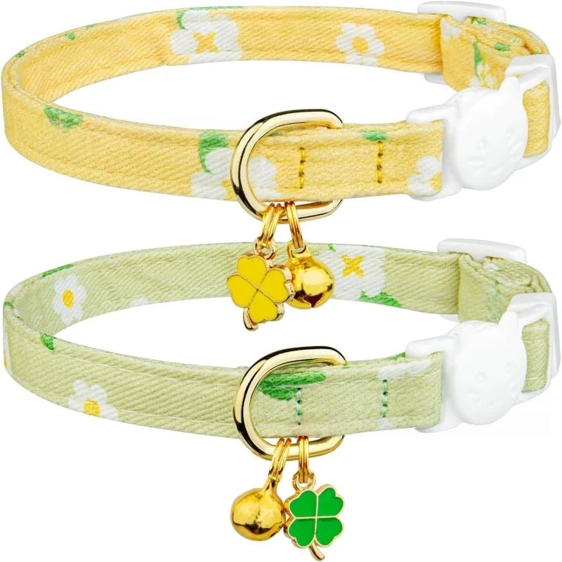 A pair of yellow floral breakaway cat collars with gold hardware and green bell tags.