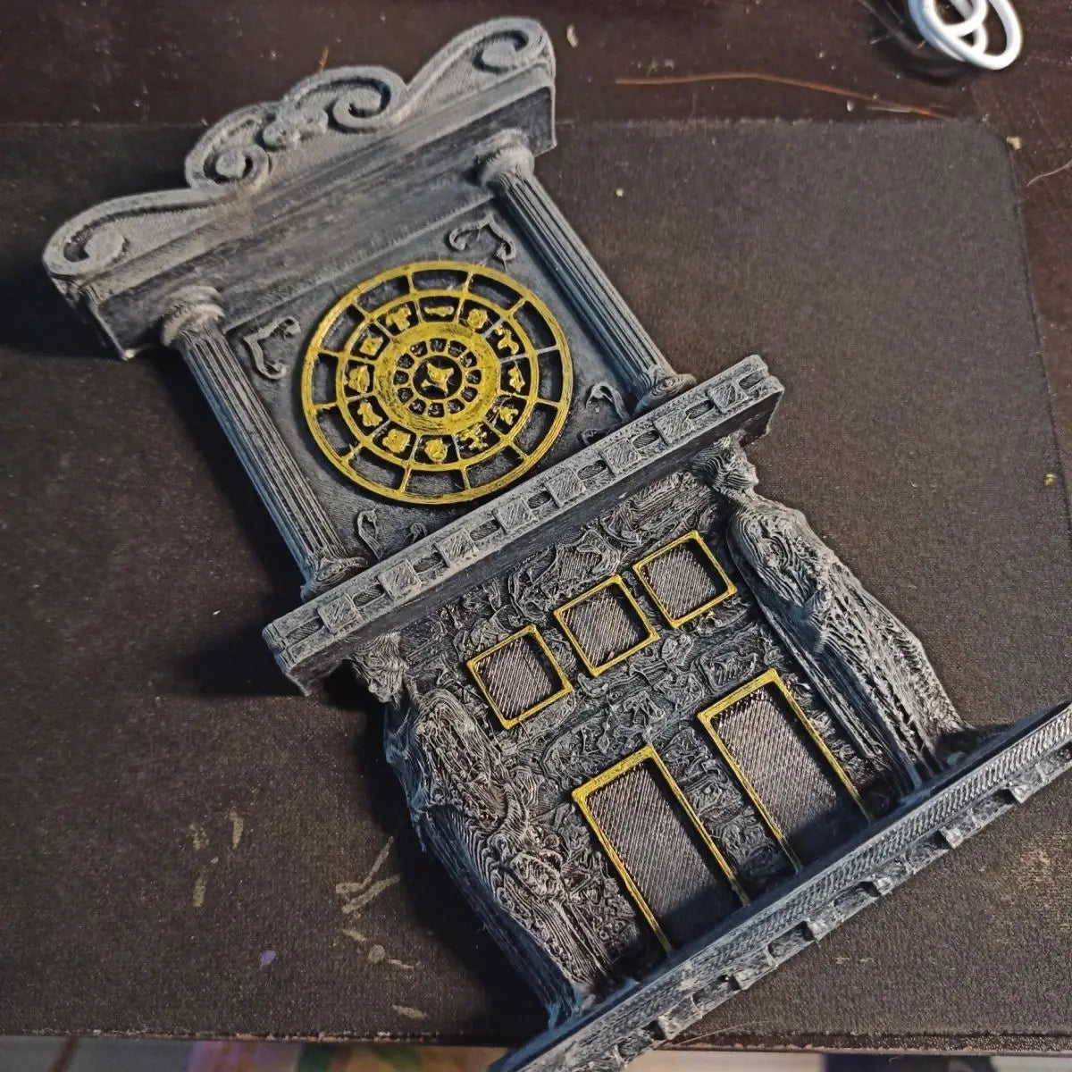Gondole de tour d'horloge imprimée en 3D avec un cadran circulaire doré orné sur une structure de pierre grise.