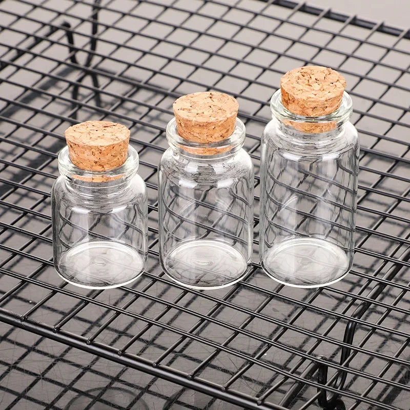 Ten mini glass bottles with cork stoppers resting on a black wire grill.