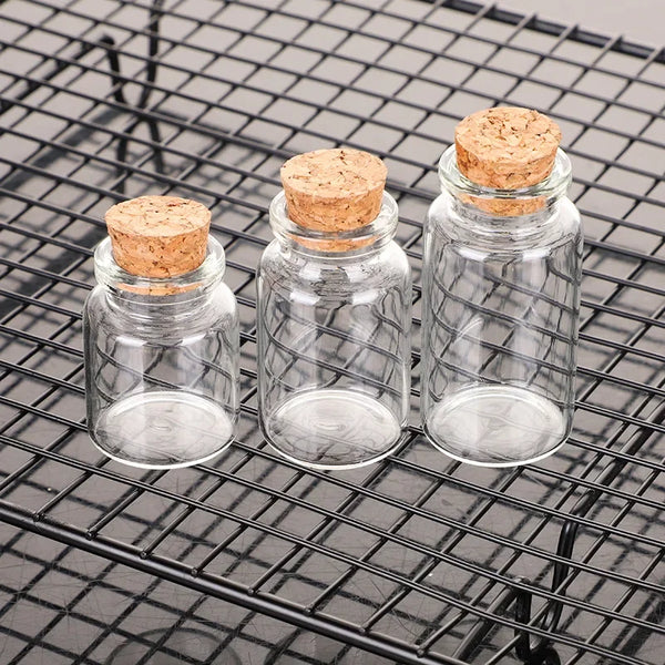 Ten mini glass bottles with cork stoppers resting on a black wire grill.