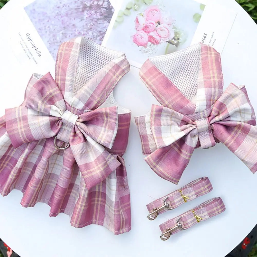 A pink and white plaid reusable dog harness dress with a bow shown on a white background.