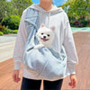 A person wearing a white hoodie is carrying a small white dog in a light blue hands-free pet sling carrier.