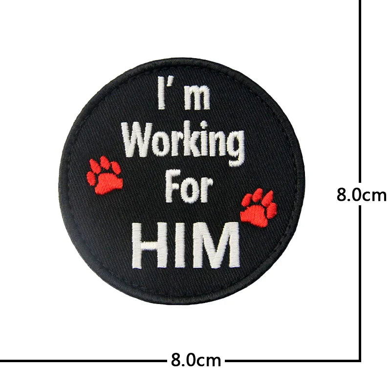 Black embroidered patch with white text I'm Working For HIM and red paw prints.