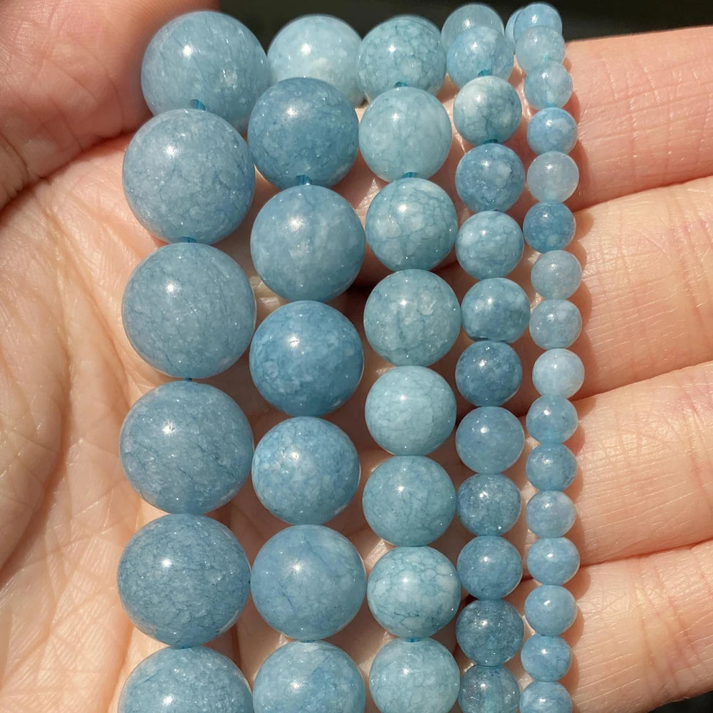 A hand holds a strand of light blue natural stone beads for jewelry making