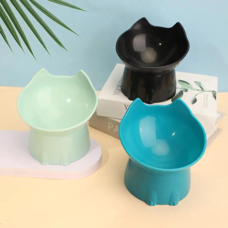 A teal elevated cat bowl with a matching base is shown next to a black version on a light surface.