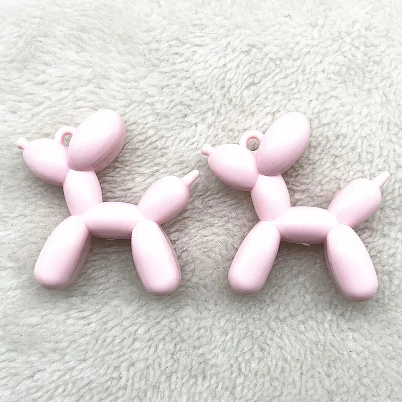 Two pink acrylic balloon dog charms displayed on a white fuzzy surface.