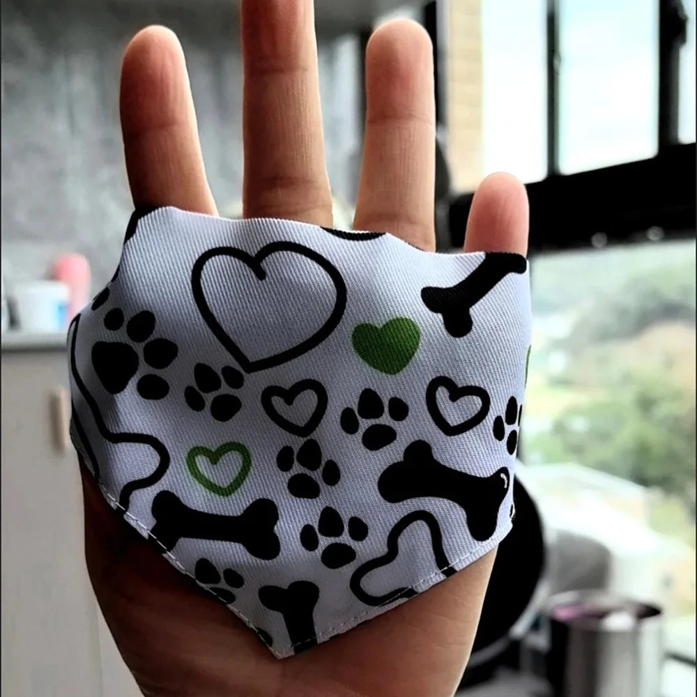 A hand holds a patterned fabric bandanna with paw prints and bone shapes for small pets