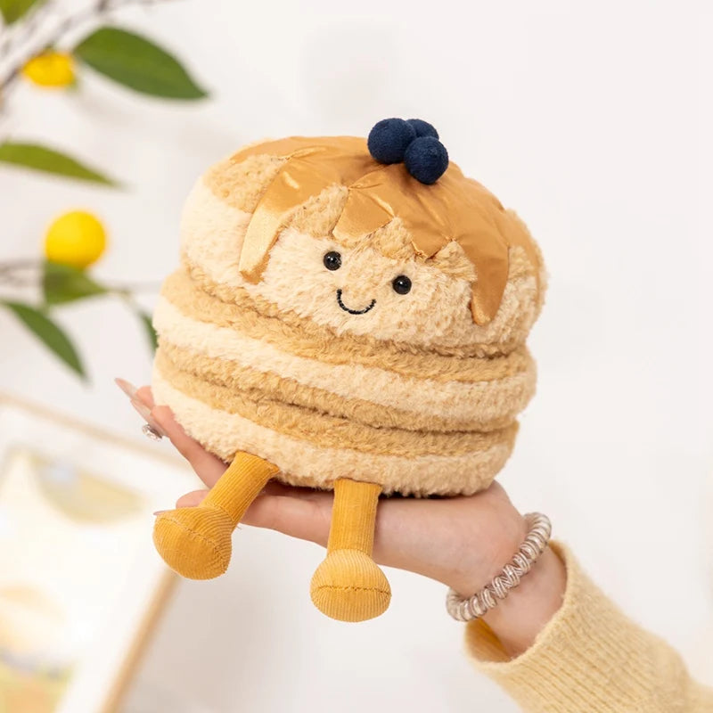 A fluffy, light brown dessert plush toy with gold accents and a dark blue bow being held in a hand.