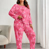 A woman models a pink heart print pajama set featuring hearts on a long-sleeved top and matching pants.
