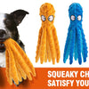 A dog is playing with an orange squeaky chew toy, next to plush octopus toys in yellow, blue, and purple.
