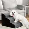A fluffy white dog is standing on a black and gray memory foam pet ramp in a living room setting.