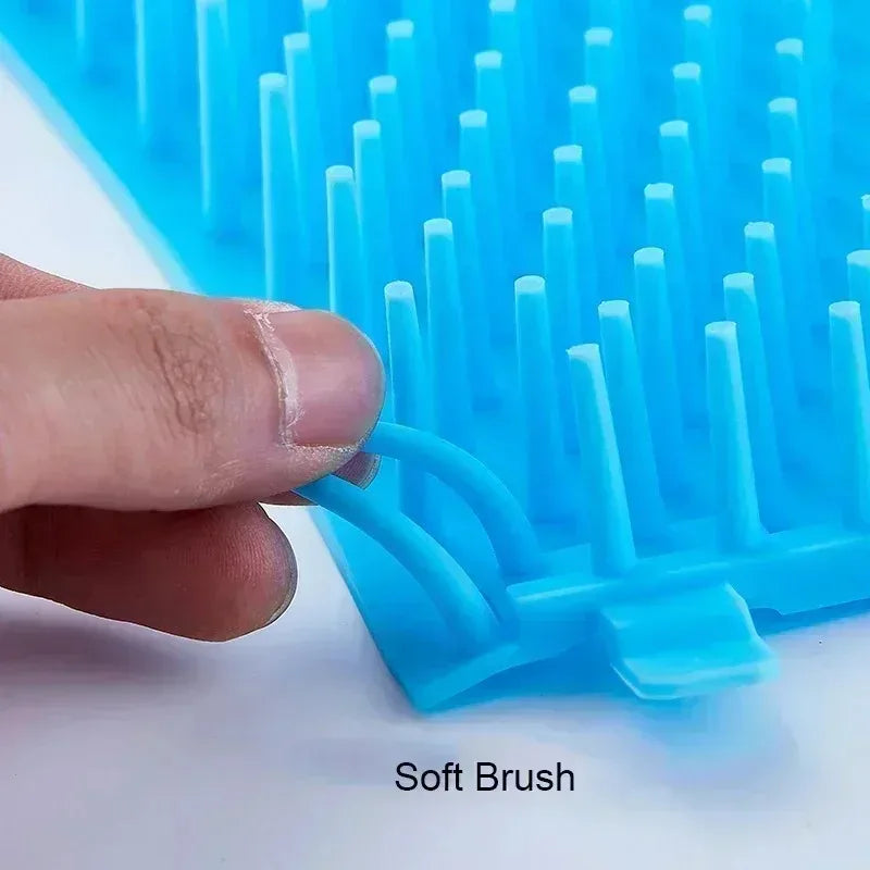 A hand is holding a blue silicone brush with soft bristles against a white background.
