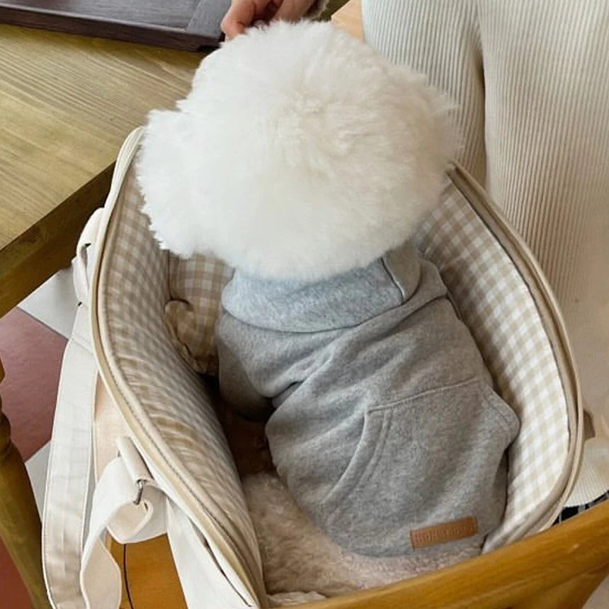 Un pull en polaire pour chien confortable avec un pompon blanc duveteux, montré dans un panier tissé de couleur claire.