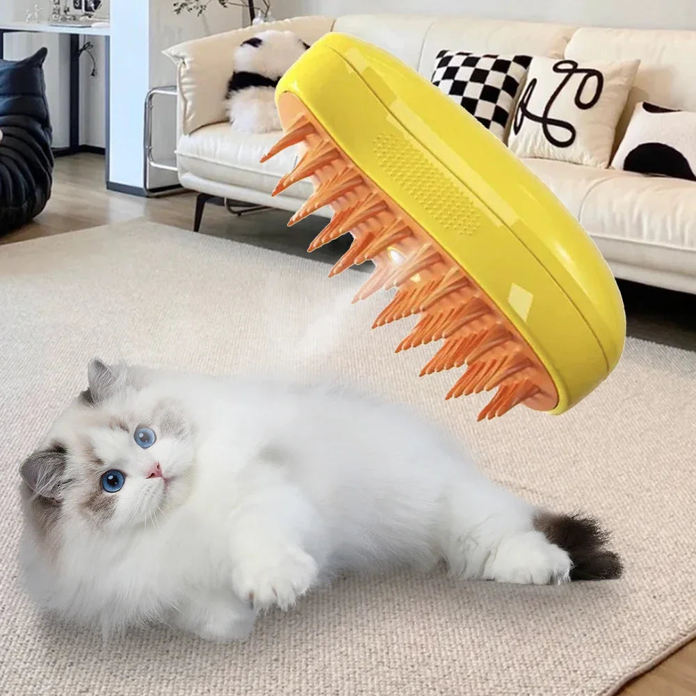 A fluffy white kitten is lying on a light rug near a yellow pet grooming brush with orange bristles and steam spray.