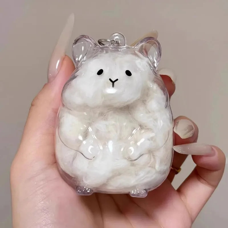 A clear resin figurine of a fluffy white hamster with large ears being held in a hand.