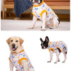 A dog wearing a light blue and yellow patterned post-surgery recovery suit.