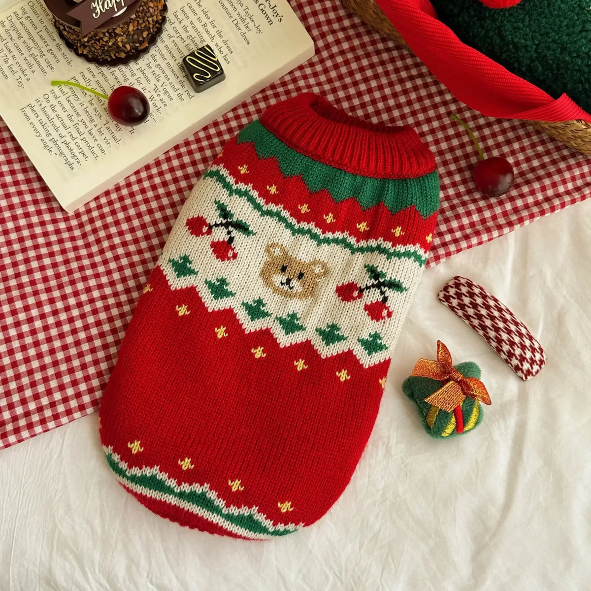A red knitted pet sweater with white trim and a brown bear design rests on a white surface.