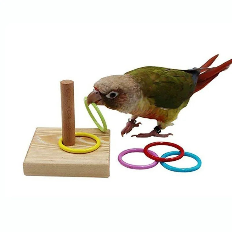 A small bird toy with a brown body and red wings is perched on a wooden block next to yellow and green rings.