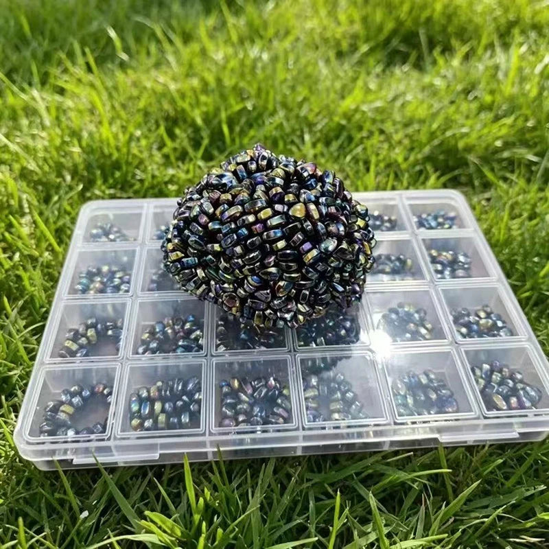A clear plastic tray filled with colorful stone cobblestone beads resting on green grass.