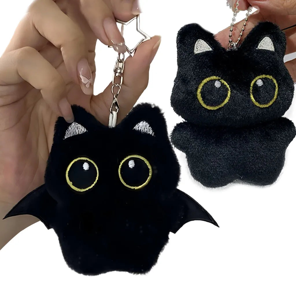 A black cat plush pendant with gold accents is being held by a hand, showing its soft texture and detail.