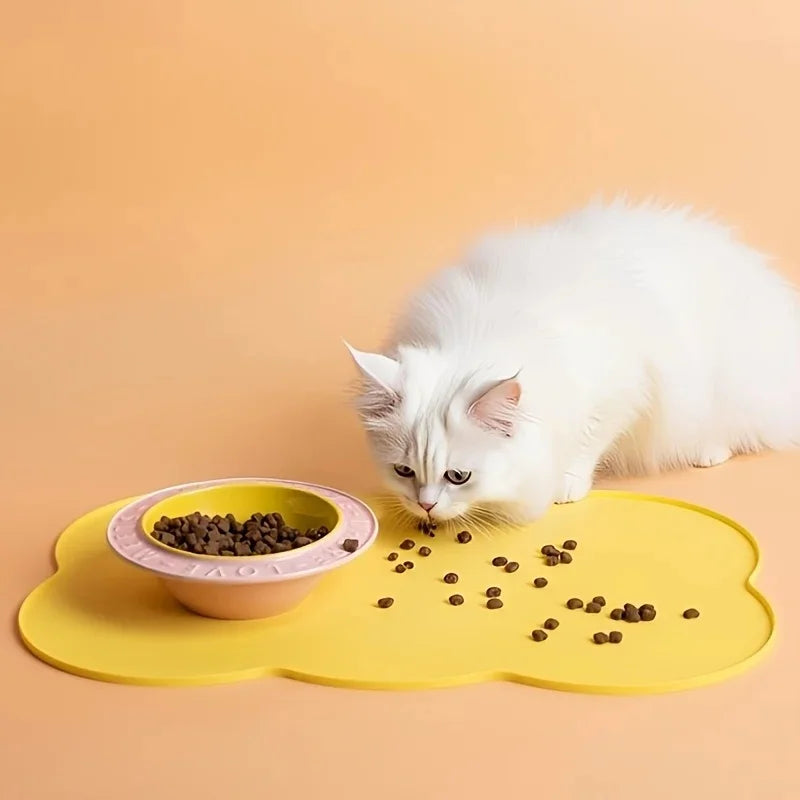 A white cat is eating dry food from a yellow silicone pet feeding mat.