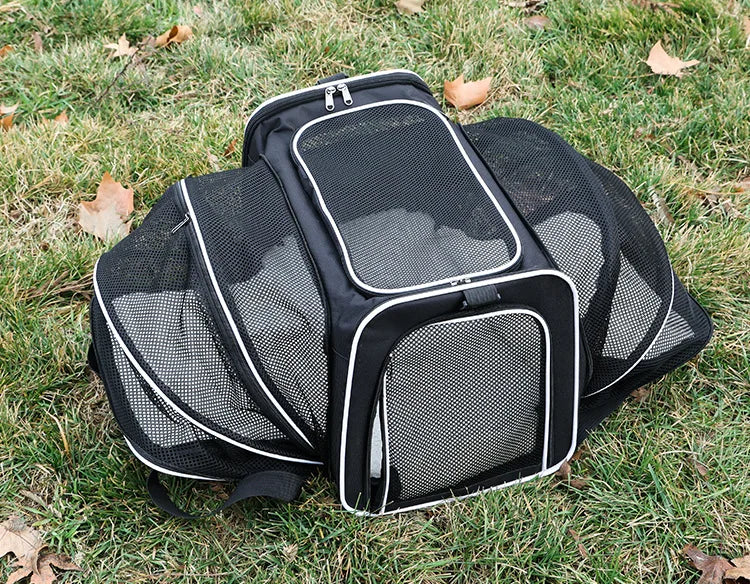 A black foldable soft-sided pet carrier with mesh panels lying on green grass.