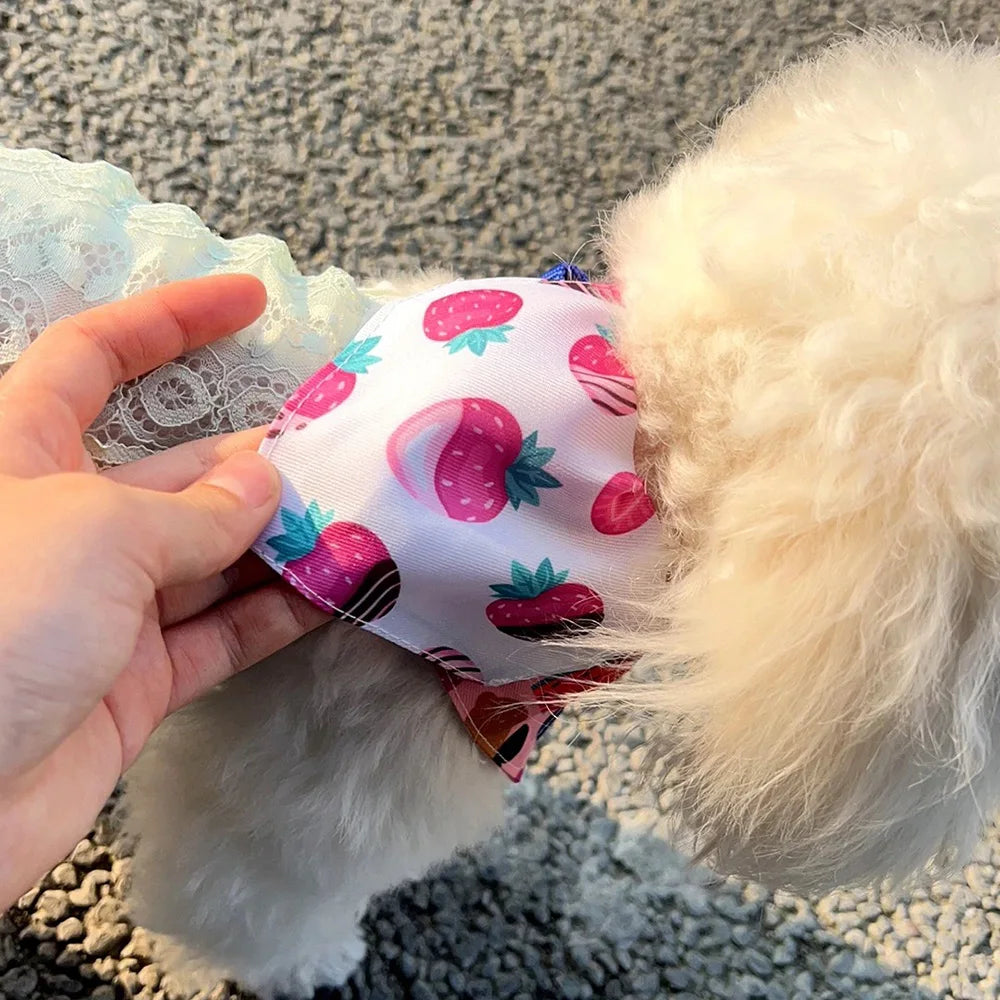 A pink and green sweet print triangle collar bandana is being held by a hand against a fluffy white dog's fur.