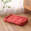 A rectangular, bright coral-colored faux fleece pet sofa bed with a waterproof base lying on a wooden floor.