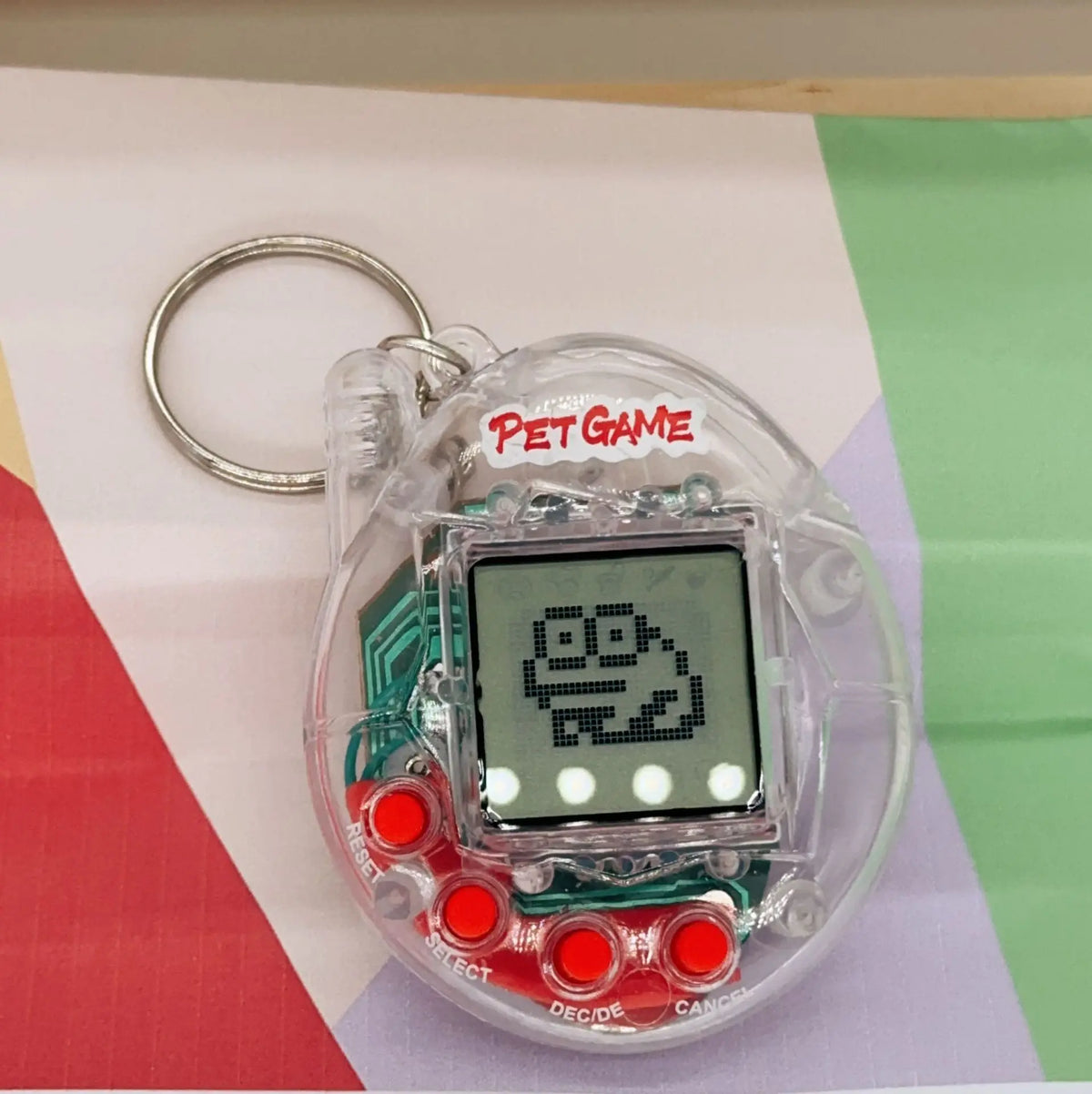 A clear plastic digital pet toy with a silver keyring and an LCD screen displaying a simple drawing.