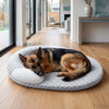 A dog is lying on a round, gray cooling ice silk pet mat indoors on a wooden floor.