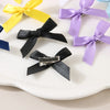 A collection of colorful ribbon bow hair clips in yellow, purple, and blue are displayed on a white surface.