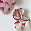 Weißer Hoodie mit roten Herzdrucken und rosa Futter, gefaltet auf weißem Untergrund.