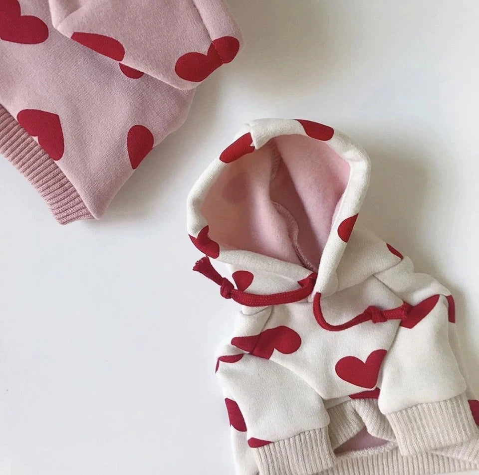 Weißer Hoodie mit roten Herzdrucken und rosa Futter, gefaltet auf weißem Untergrund.
