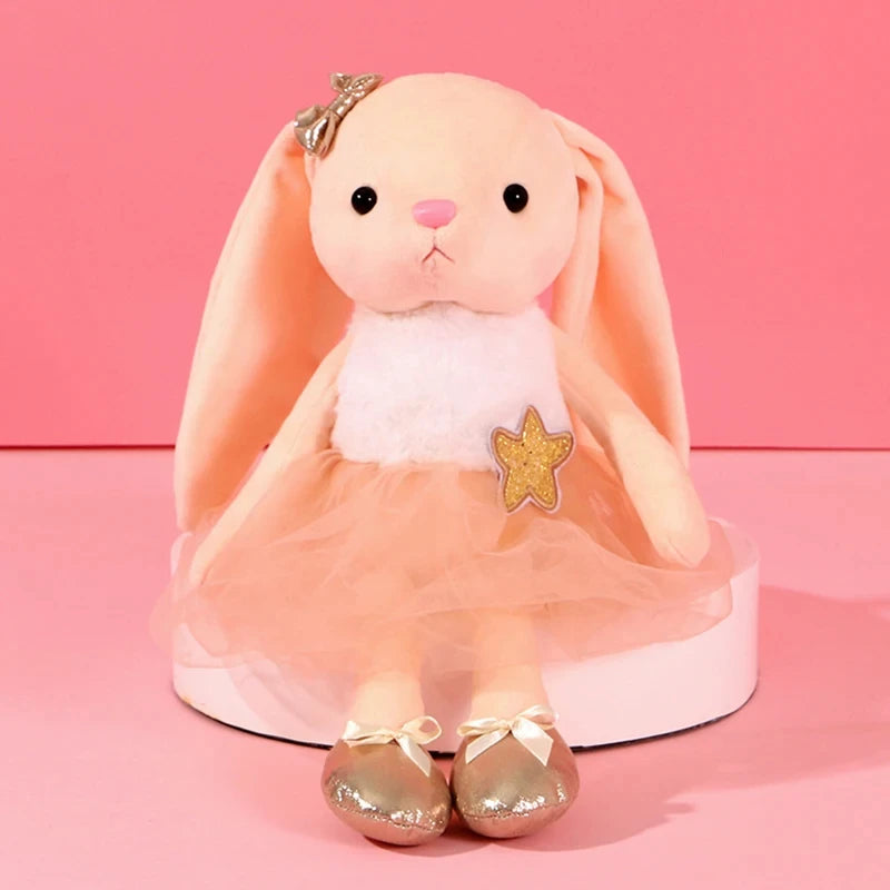 A soft peach colored plush rabbit toy with pink ears and a gold star decoration.