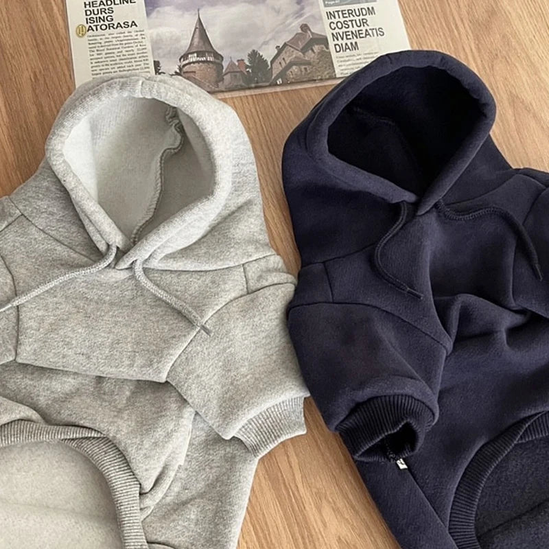 Un pull douillet gris pour chien et un hoodie bleu marine foncé sont présentés sur une surface en bois.