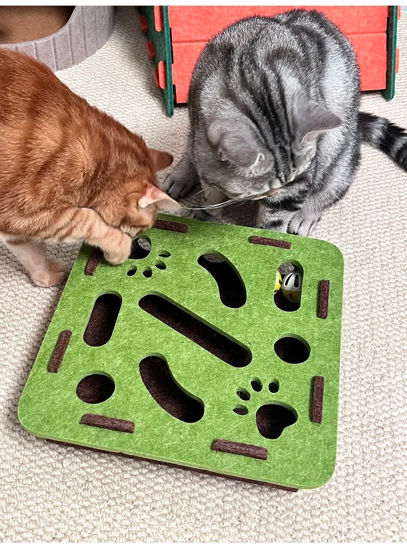 Un labyrinthe de puzzle en feutre vert pour chats avec des trous et une cloche, à côté de deux chats.