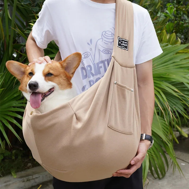 Eine Person hält einen beigen, leichten Hundeträger-Crossbody-Sling mit einem braun-weißen Hund im Freien.