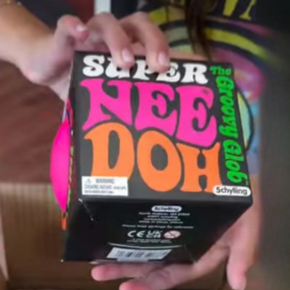 A hand holds a box of Super Nee Doh Groovy Glob stress ball toy.