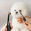 A person is using a black pet tear stain remover brush on a white dog with fluffy fur.